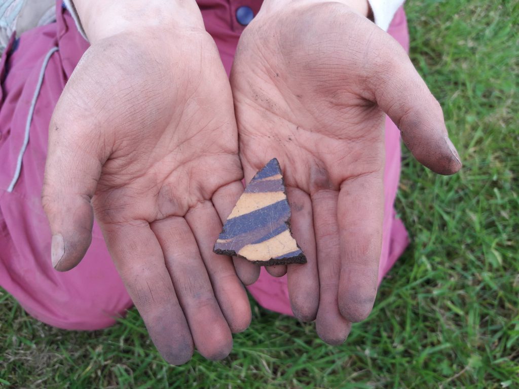 Young archaeologist holding yellow and brown pot sherd