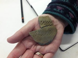 A hand holding fragments of decorated medieval pottery
