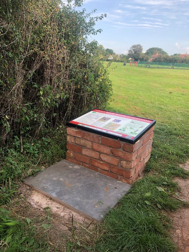 Interpretation panel on a brick stand with open green space behind.