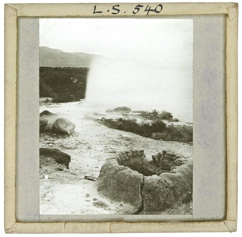 Glass slide showing former geyser in foreground and spray of water behind
