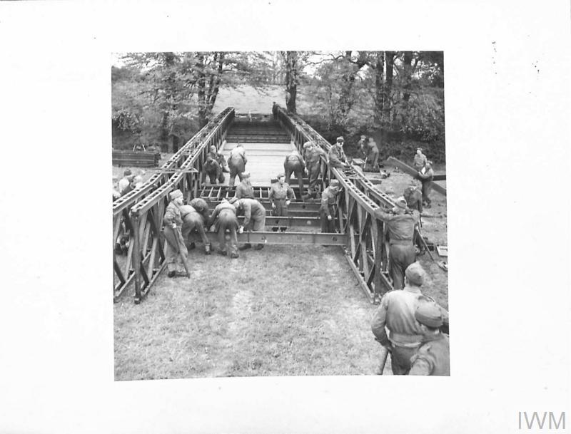 Soldiers building a bridge over water with trees beyond