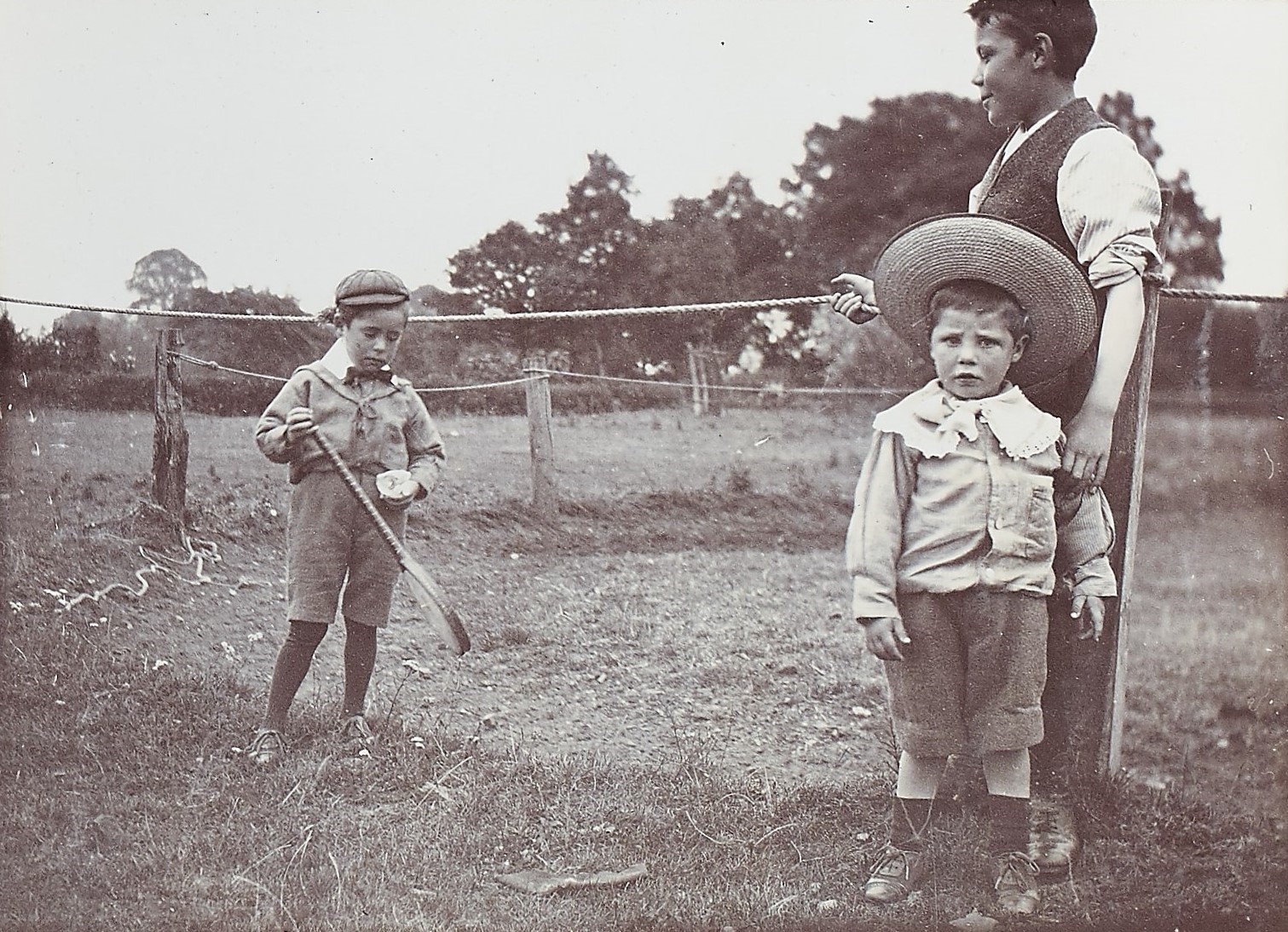 Black and white photograph of three children wearing hats stood outside in a field
