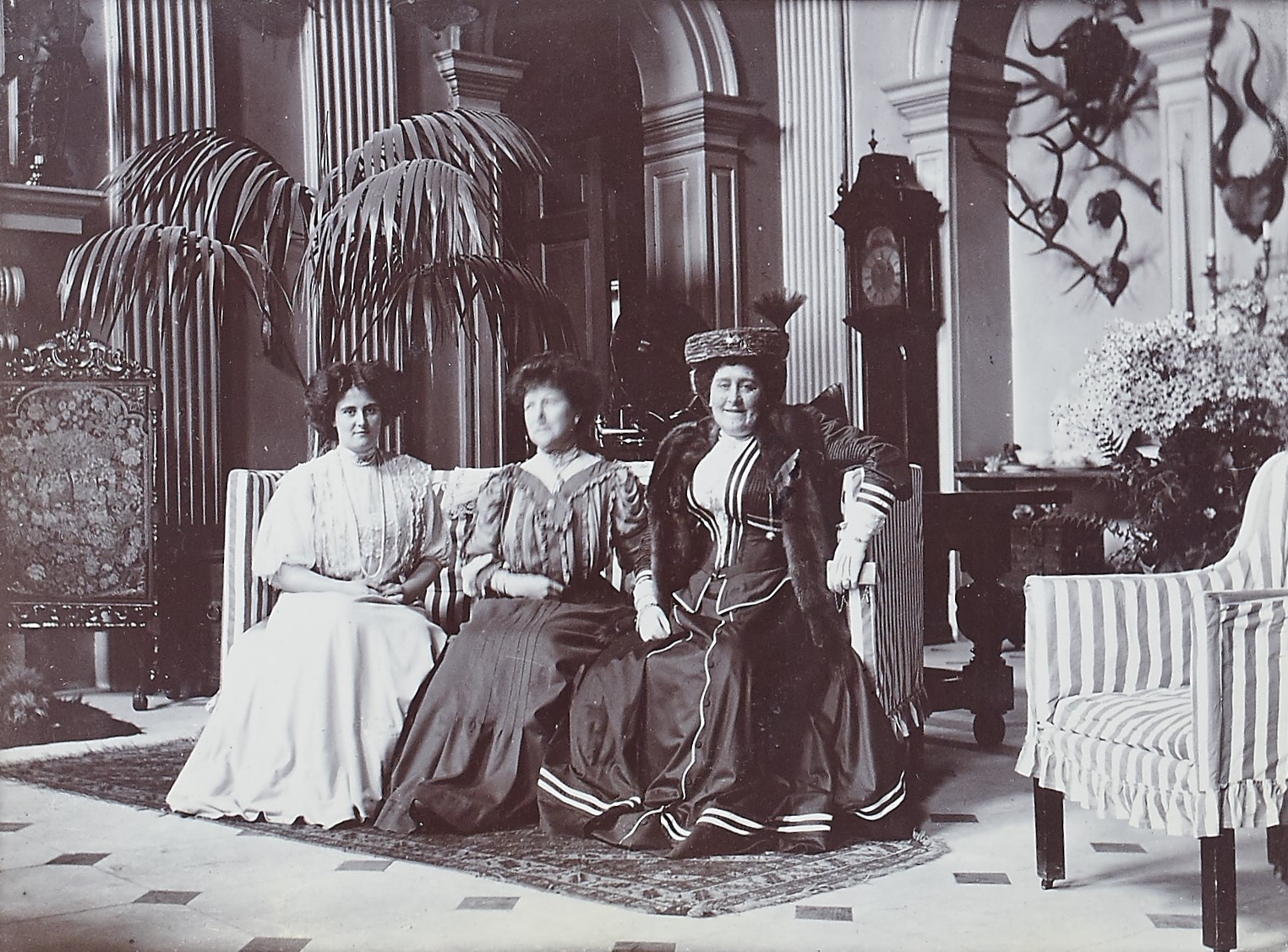 Black and white photograph of three people sat on a sofa in a grand hall
