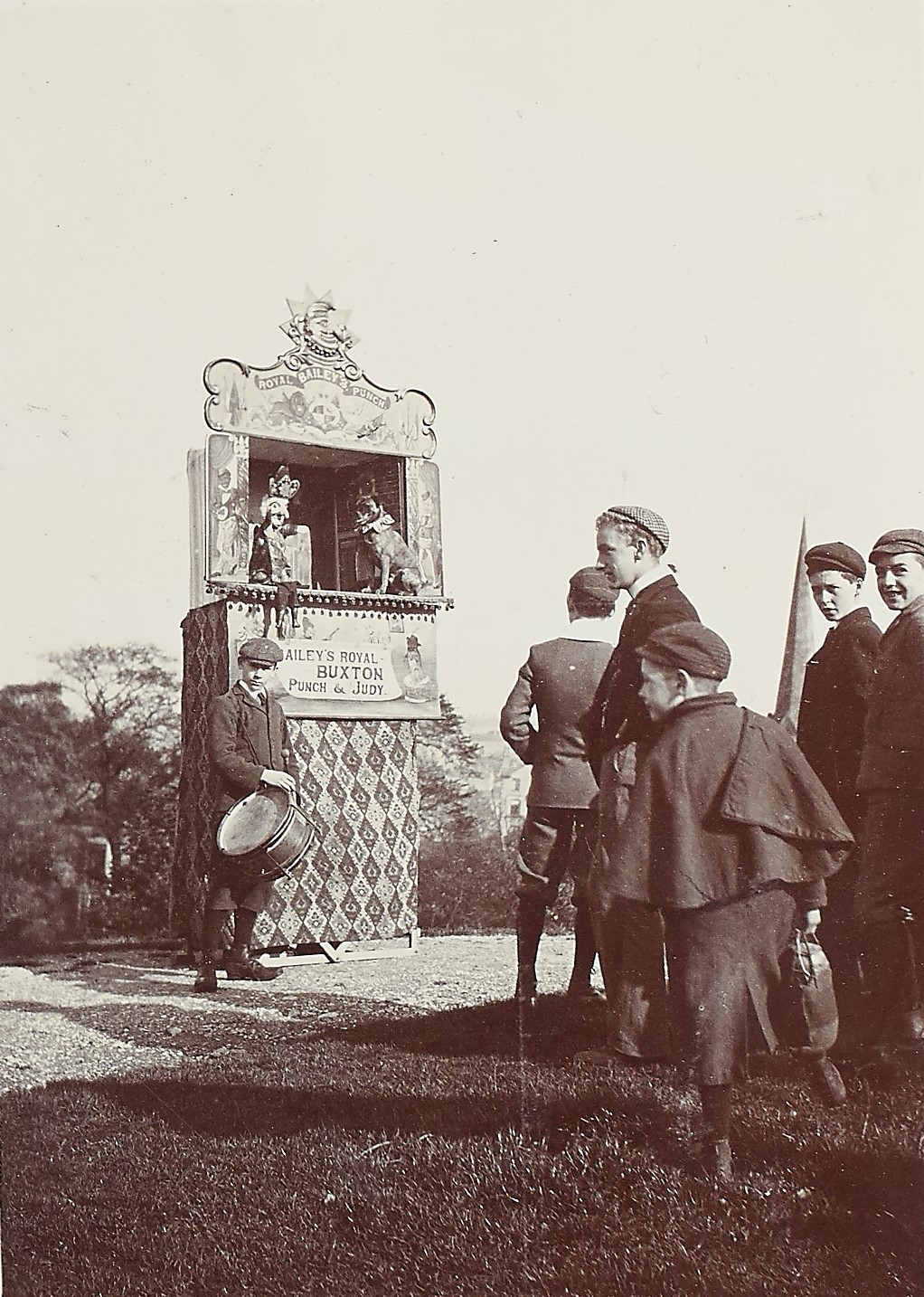 Black and white photograph of a group of people stood outside watching a puppet show