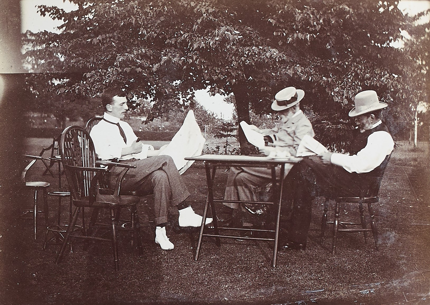 Black and white photograph of a group of people sat on chairs outside reading
