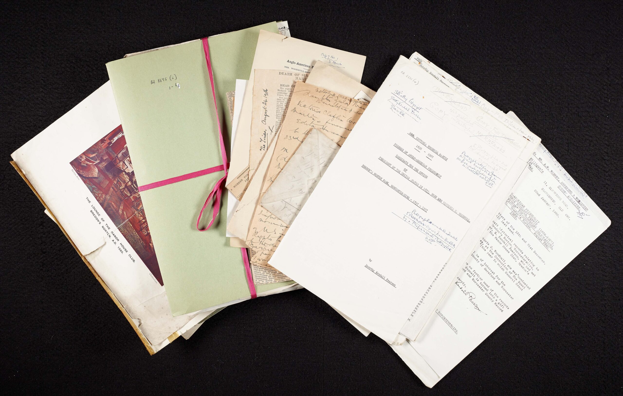 BA 8695, a collection of documents re Victoria Woodhull Martin held by Worcestershire Archives, including a green folder and many letters etc. fanned out in as rainbow pattern, black surface in background.